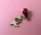 Two bird-shaped pins on a pink background