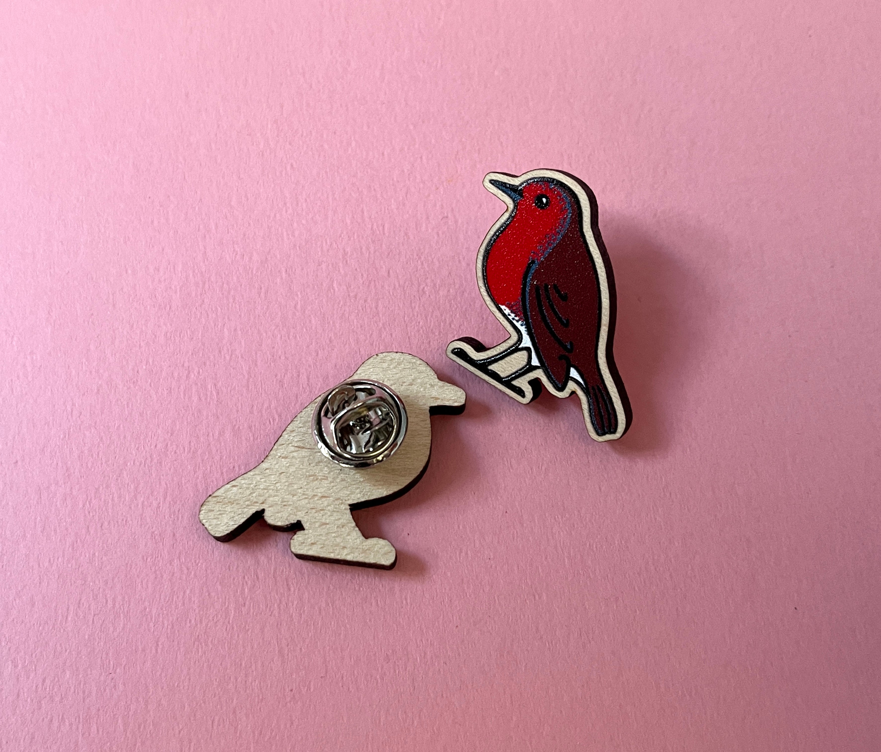Two bird-shaped pins on a pink background