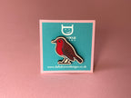 Robin badge on a teal card with a logo and website text, against a pink background