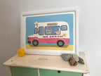 A framed illustration of a pink and white ice cream van on a light blue background. The van has the words 'Delicious' and 'Ice Cream' on it, along with a smiling sun.  The ice cream van is depicted with various ice cream cones and cups inside. The illustration is in a white frame and sits on a light-colored surface with some stones nearby.
