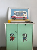 A mint green children's cabinet with two doors features appliques of playful dogs.  Atop the cabinet sits a white framed print depicting a pink and white ice cream truck on a light blue background. The words 'Ice Cream' are prominently displayed on the truck.  Small decorative stones and a yellow object resembling a small toy are also on the cabinet.