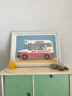 A framed illustration of a pink and white ice cream truck on a light blue background. The truck has the words 'Delicious' and 'Ice Cream' on it. The illustration is in a white frame and is sitting on a light green cabinet. There are some small decorative items on the cabinet next to the frame.