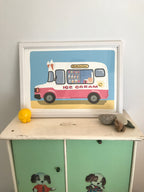A framed illustration of a pink ice cream truck on a light blue background. The truck has the words 'Delicious' and 'Ice Cream' on it.  The window displays various ice cream cones and other treats. The truck has a smiling sun decal on the side. The illustration is displayed on a light green cabinet with painted doors