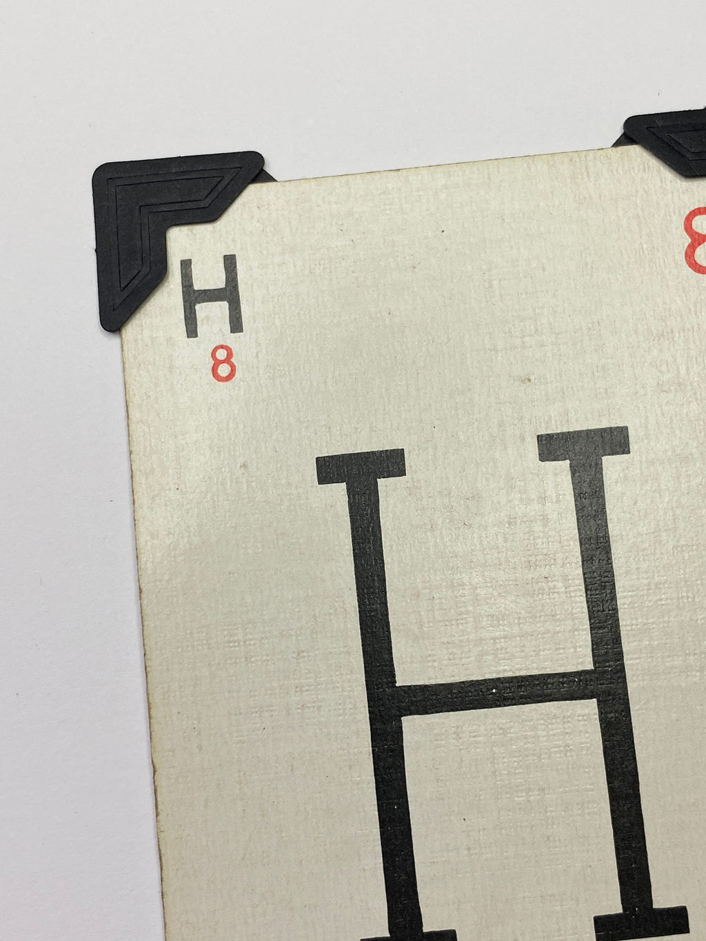 May include: A white card with a black letter H printed on it. The card has a black corner protector